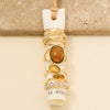A stack of assorted gold rings displayed on a white ring holder, featuring various stone and metal designs, photographed against a neutral beige background.