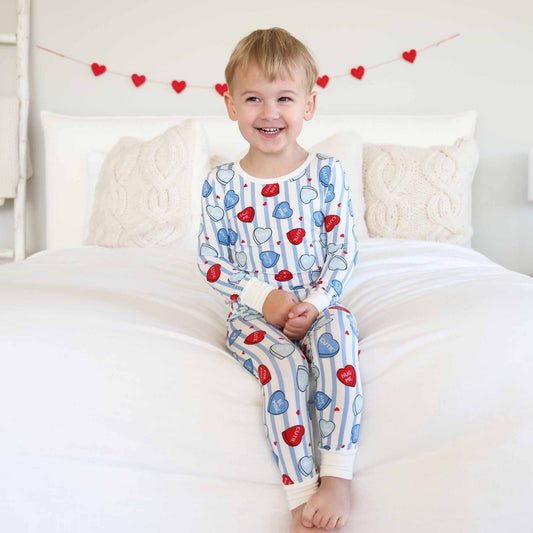 Child wearing heart-patterned pajamas sitting on a bed with decorative hearts in the background.