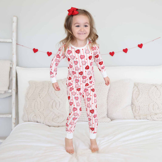 Child wearing a heart-patterned onesie standing on a bed with decorative hearts in the background.