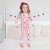 Child wearing a heart-patterned onesie standing on a bed with decorative hearts in the background.