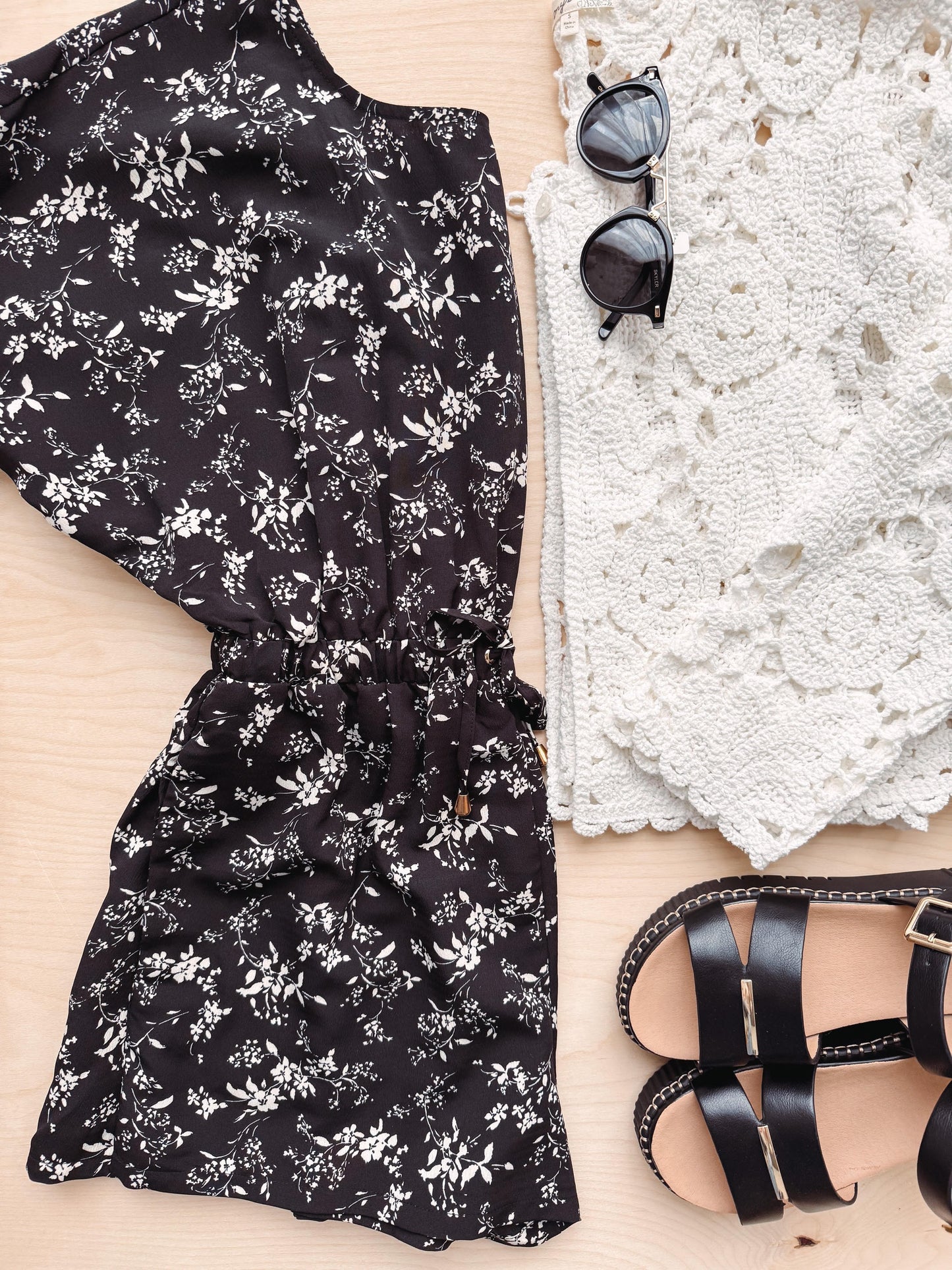 Black floral dress, sunglasses, and black sandals on a light wooden surface