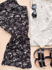 Black floral dress, sunglasses, and black sandals on a light wooden surface