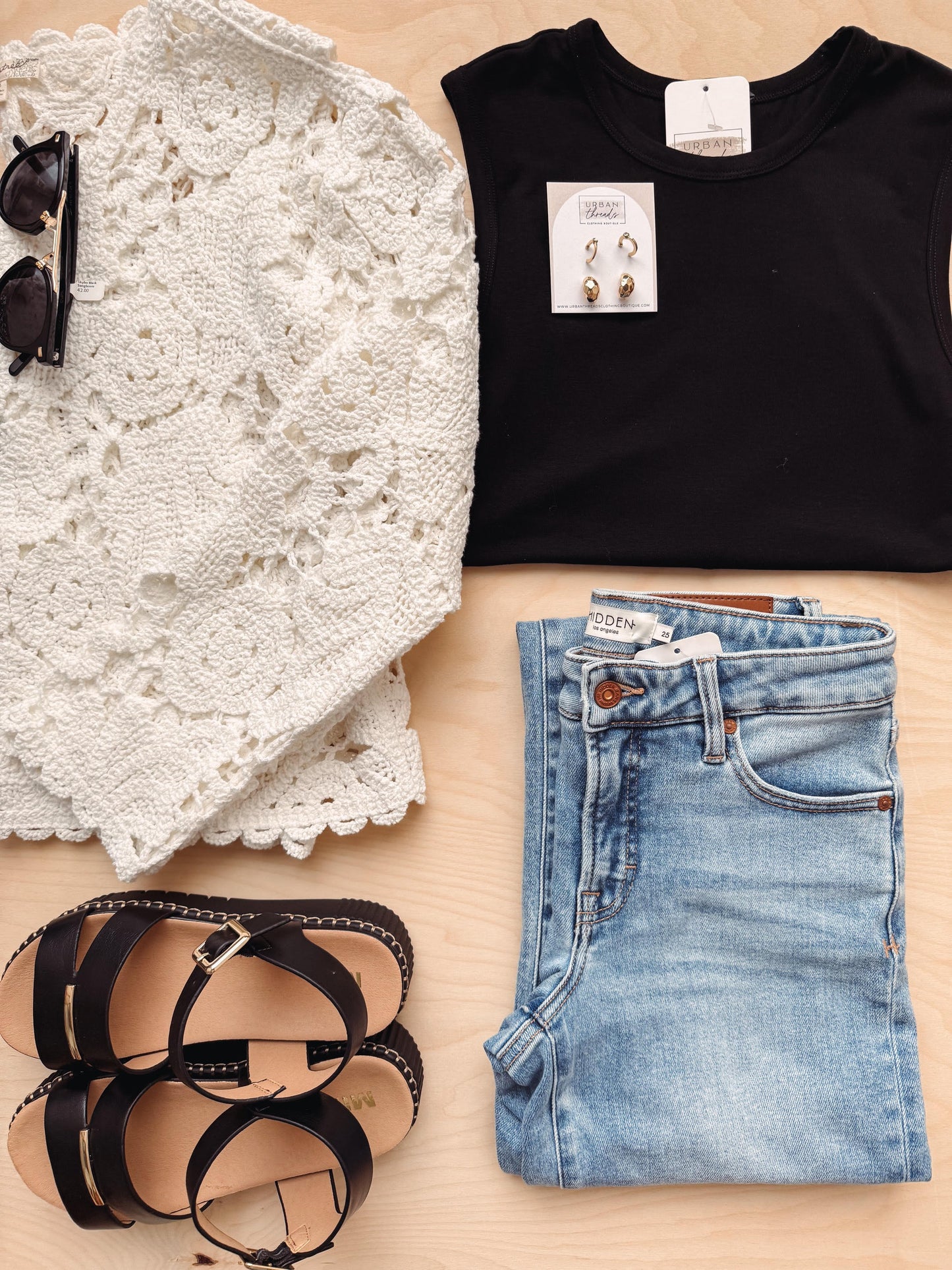 Black sleeveless top, white lace garment, black sandals, and blue jeans on a wooden surface.
