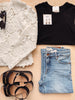 Black sleeveless top, white lace garment, black sandals, and blue jeans on a wooden surface.