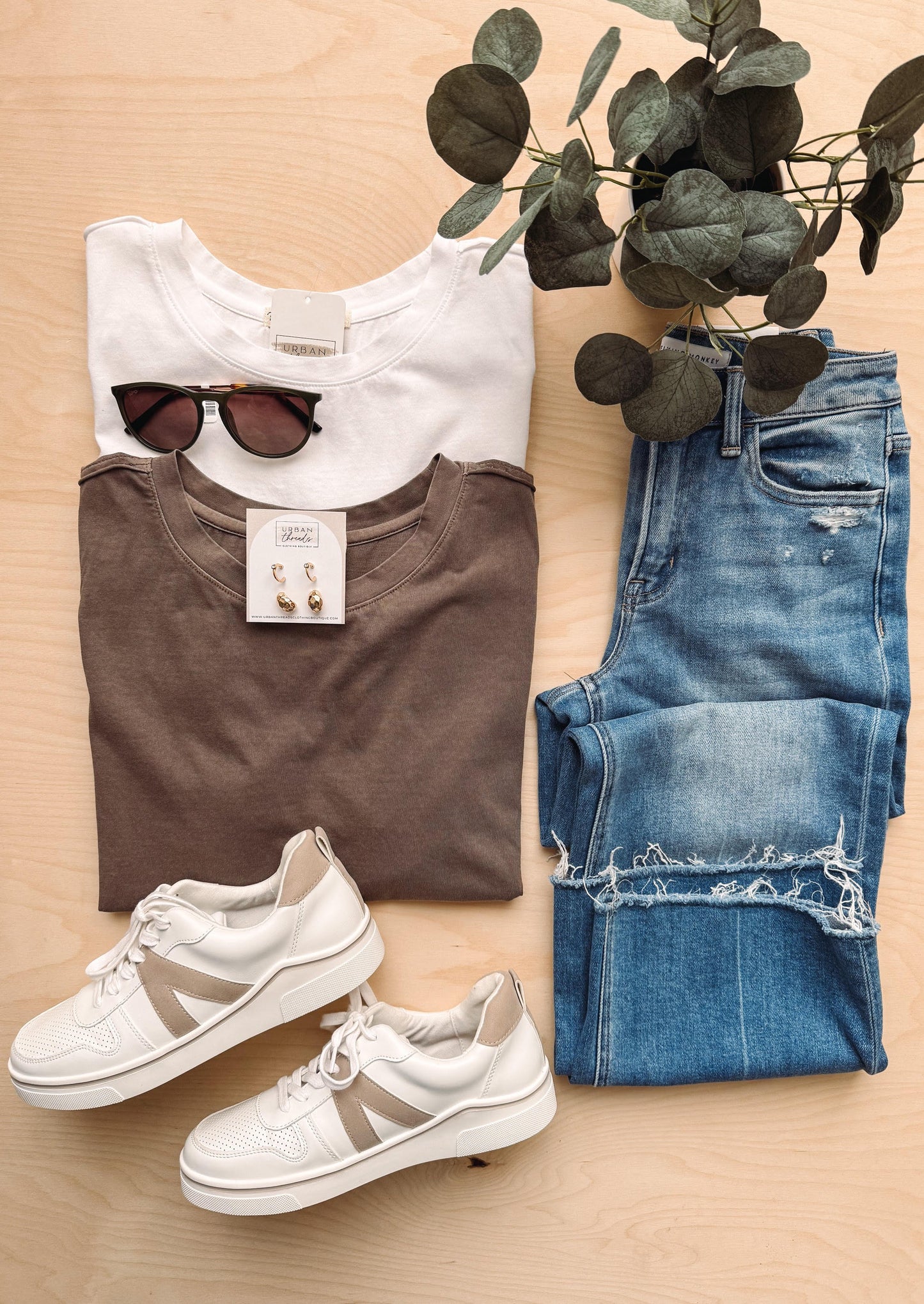 Brown t-shirt, white sneakers, blue jeans, sunglasses, and a plant on a wooden surface