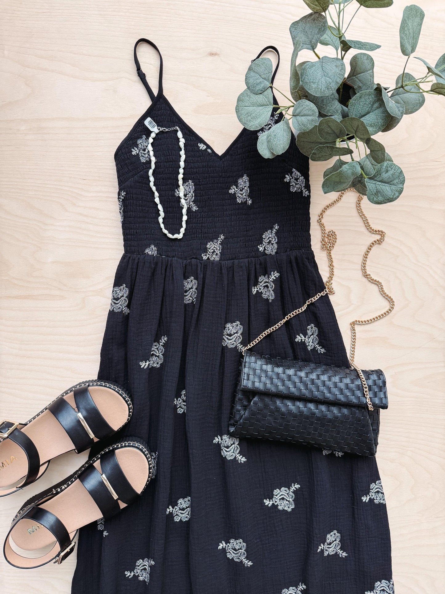 Navy blue dress with white floral patterns, sandals, and a clutch on a beige surface.