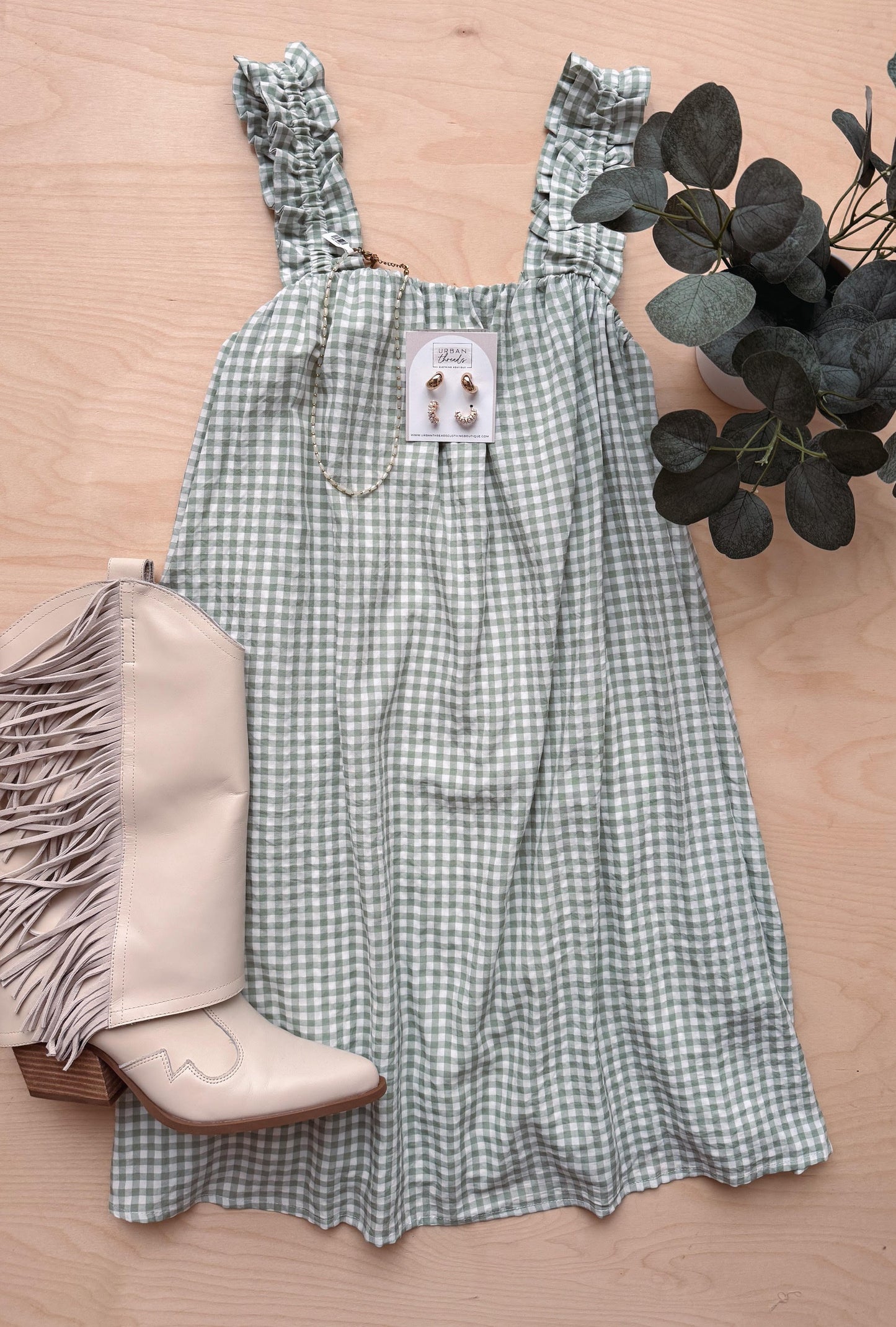 Green checkered dress with a boot and plant on a wooden surface