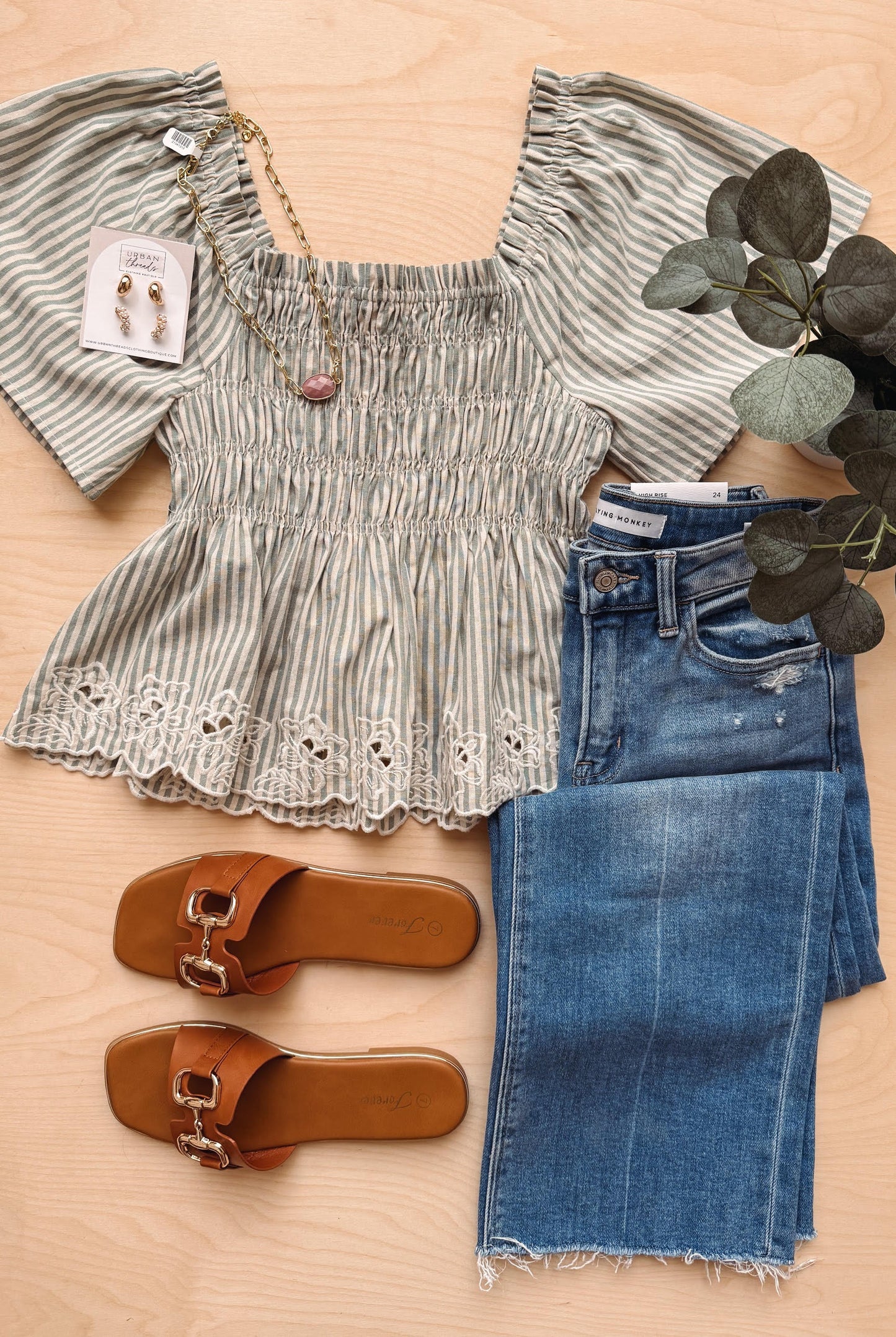 Striped top, jeans, and sandals on a wooden surface with a plant.