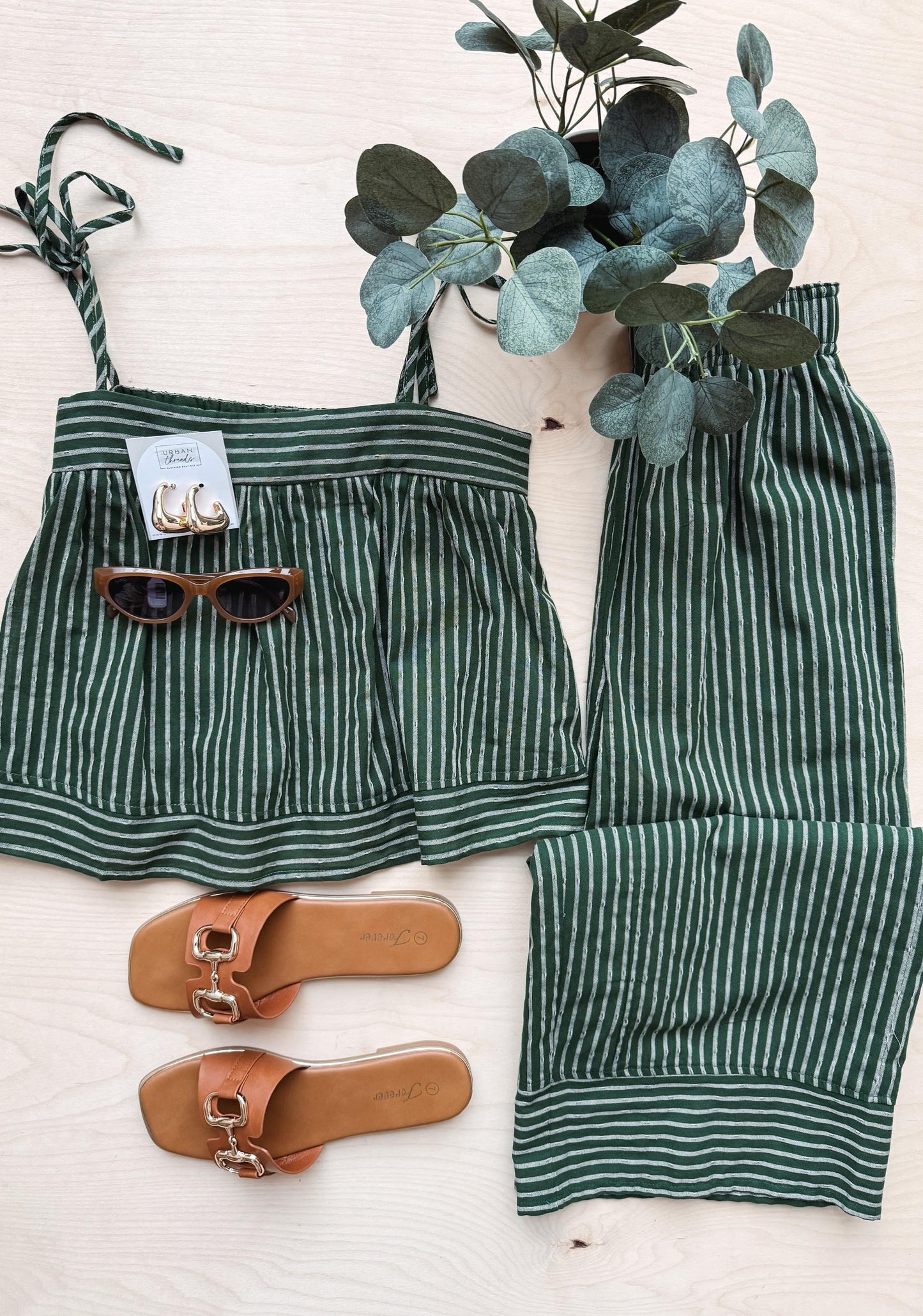 Green and white striped swimsuit with sunglasses and sandals on a light background