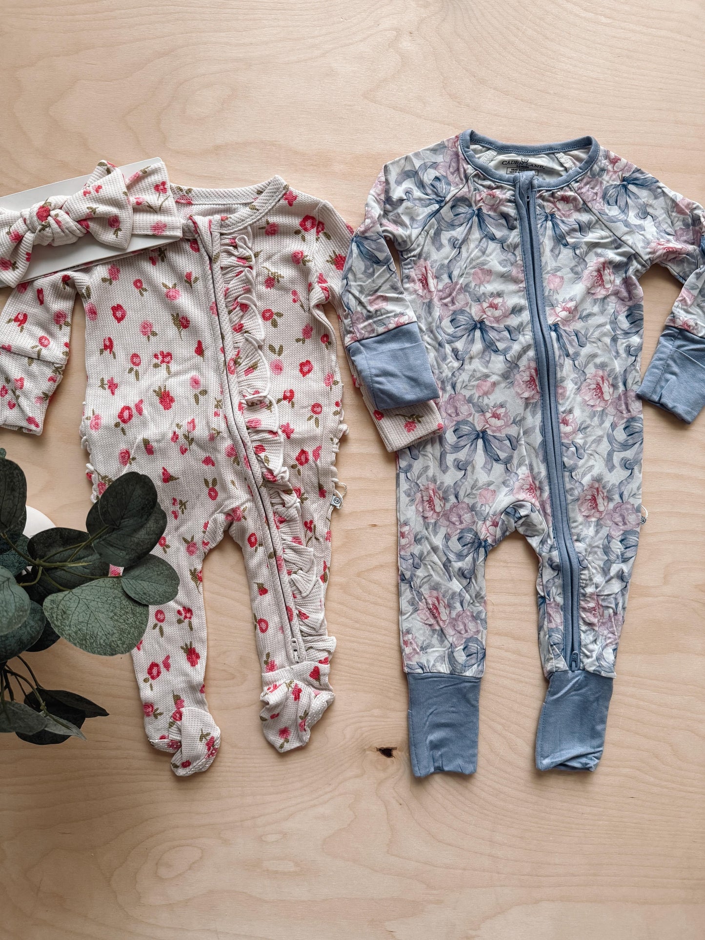 Two baby rompers with floral patterns on a wooden surface.