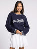 Woman wearing a navy sweater with 'Go Sports' text and a white skirt on a light gray background