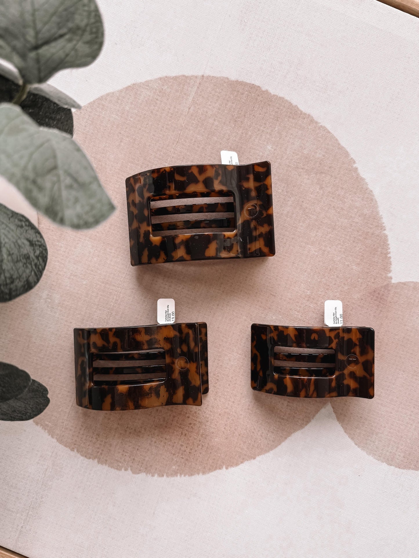 Three tortoiseshell hair clips on a decorative surface with green leaves.