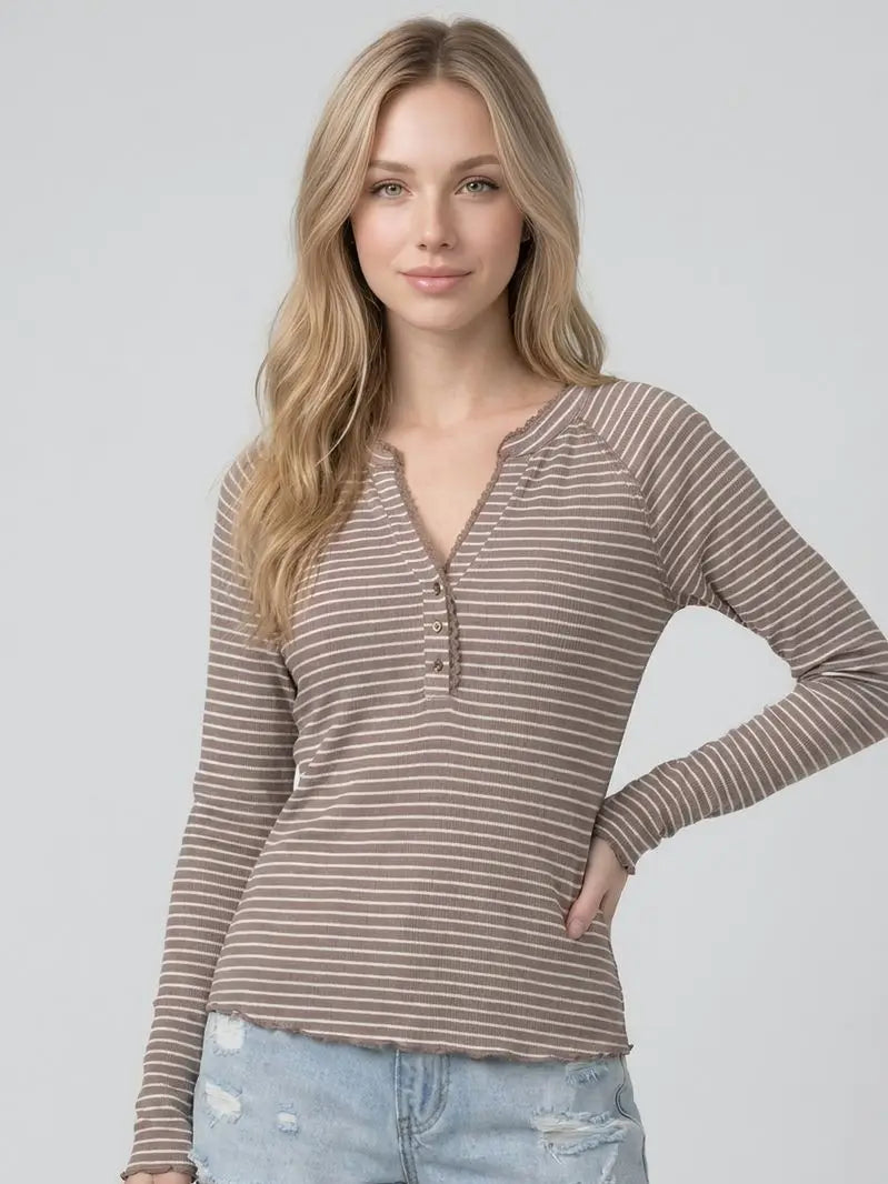 A woman modeling a long-sleeve henley top with thin brown and beige horizontal stripes, paired with light blue jeans, against a solid light gray background.