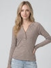 A woman modeling a long-sleeve henley top with thin brown and beige horizontal stripes, paired with light blue jeans, against a solid light gray background.