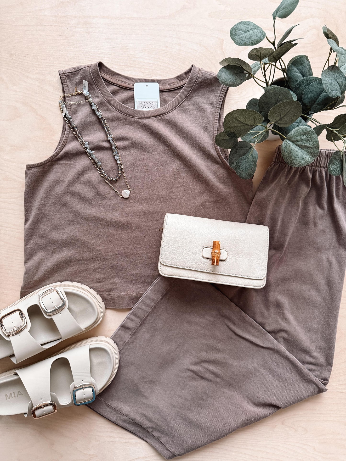 Brown tank top and shorts set with a white sandal, clutch, and necklace on a light wooden surface.