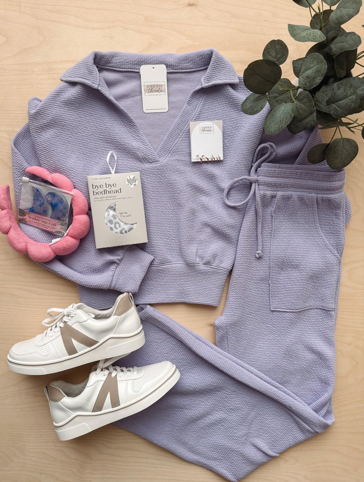 Purple tracksuit with white sneakers on a wooden surface, accompanied by a plant.