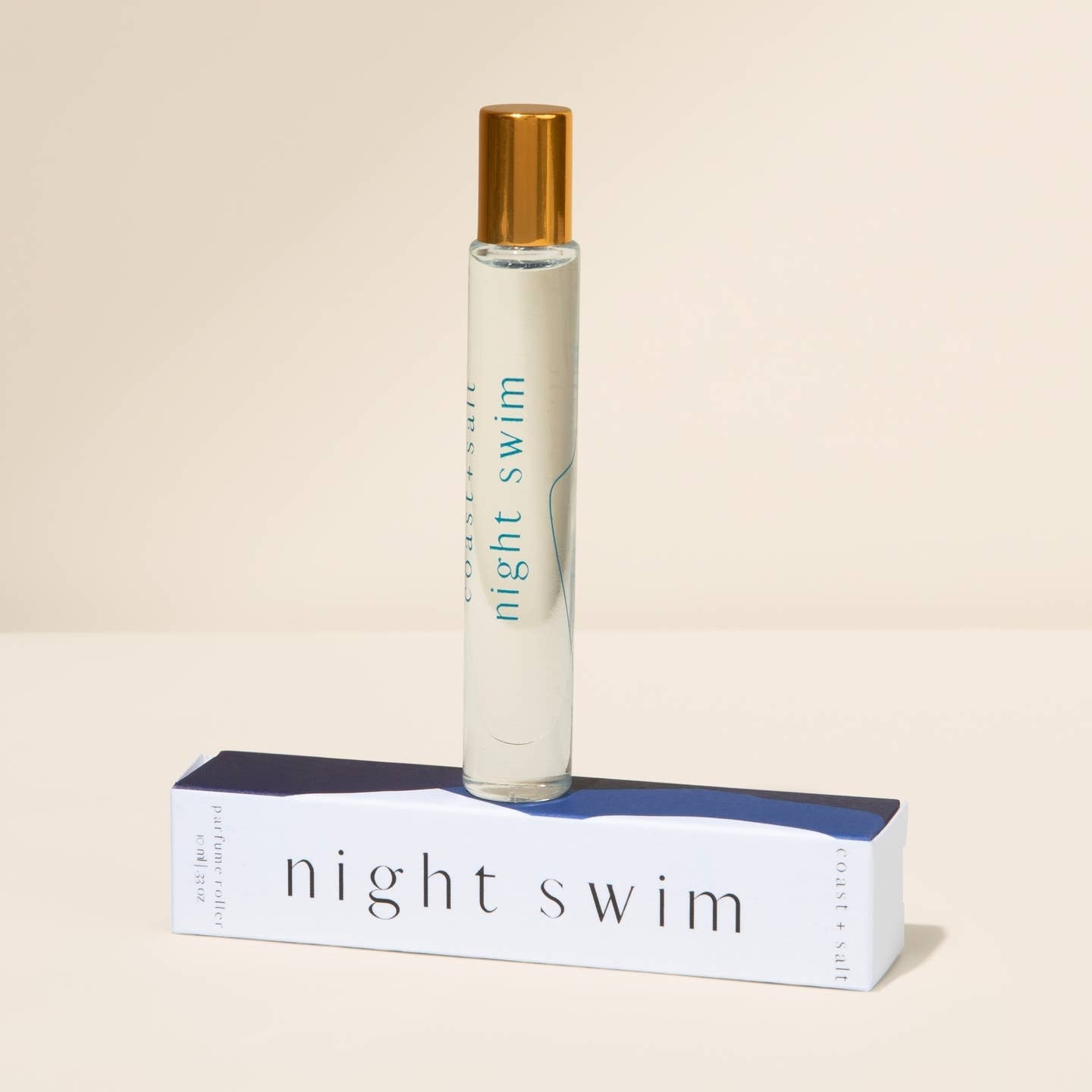 Roll-on bottle of 'night swim' with gold cap on a beige background