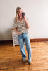 Woman taking a mirror selfie wearing a striped shirt and jeans in a room with wooden flooring.