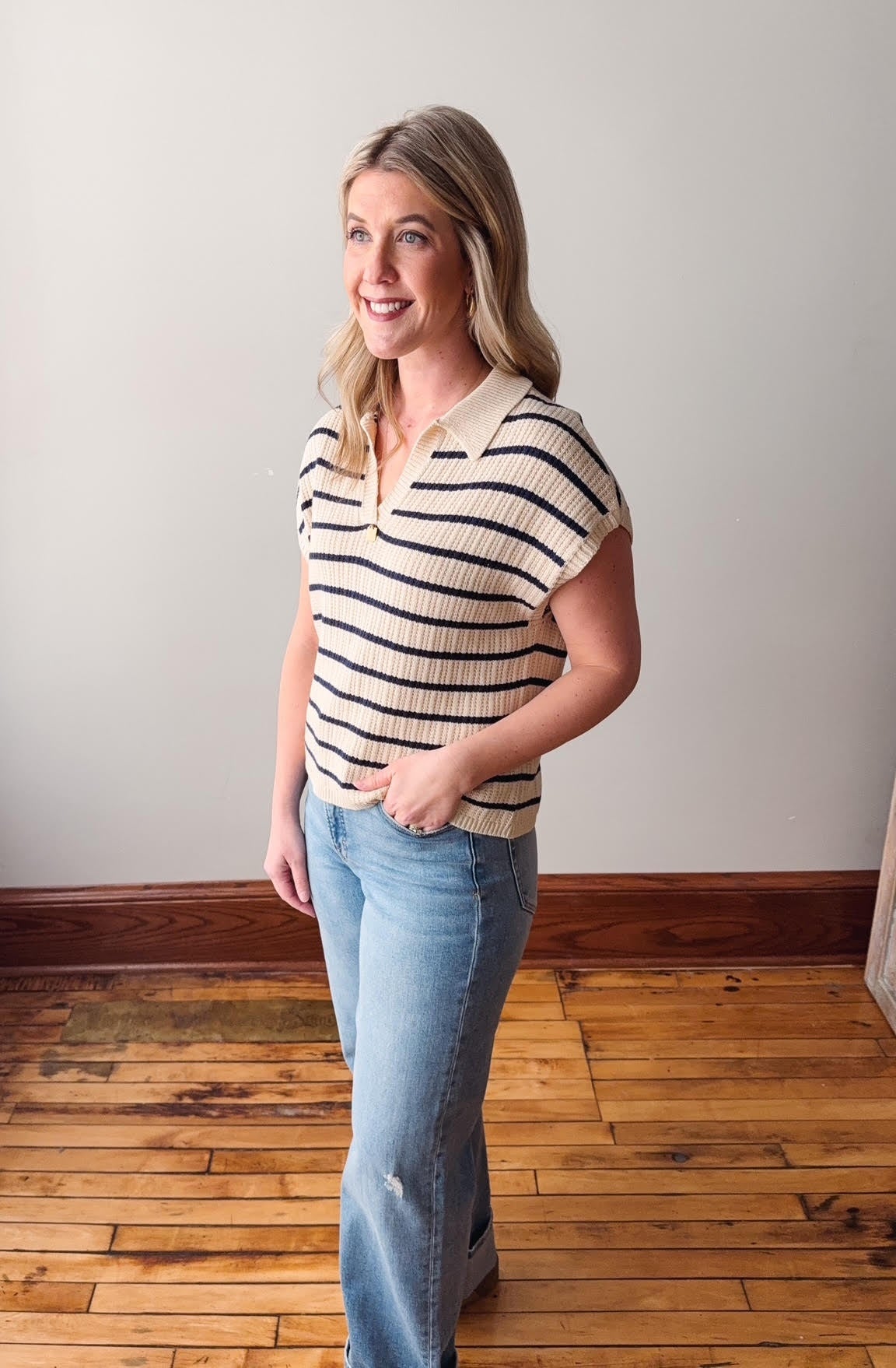 Woman wearing a striped shirt and jeans standing on a wooden floor.