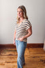 Woman wearing a striped shirt and jeans standing on a wooden floor.