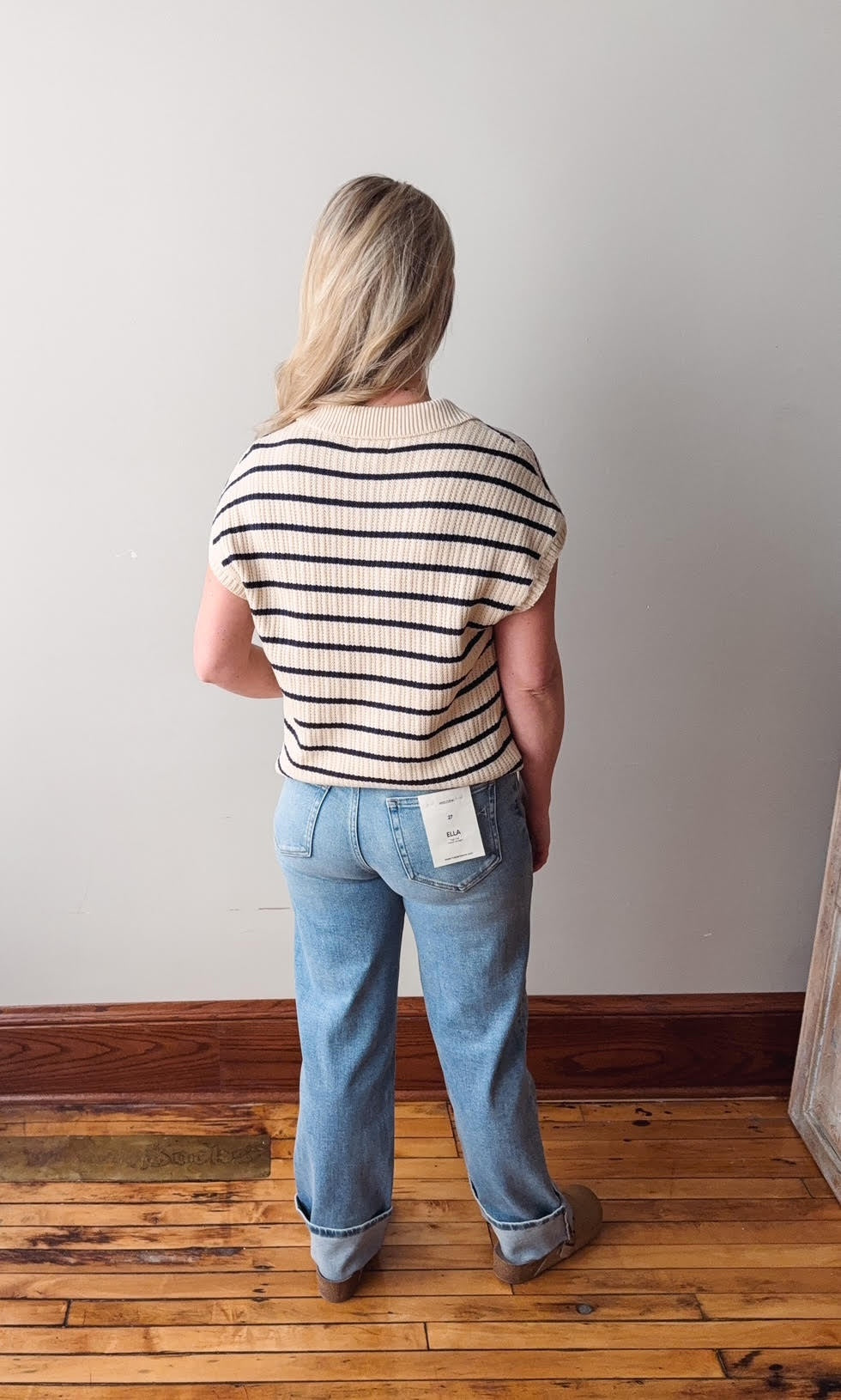 Person wearing a striped shirt and blue jeans standing against a plain wall.