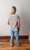 Person wearing a striped shirt and blue jeans standing against a plain wall.