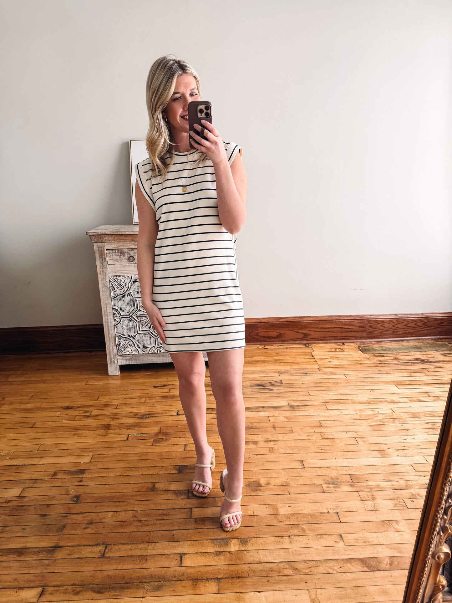 Woman taking a mirror selfie wearing a striped dress in a room with wooden flooring.