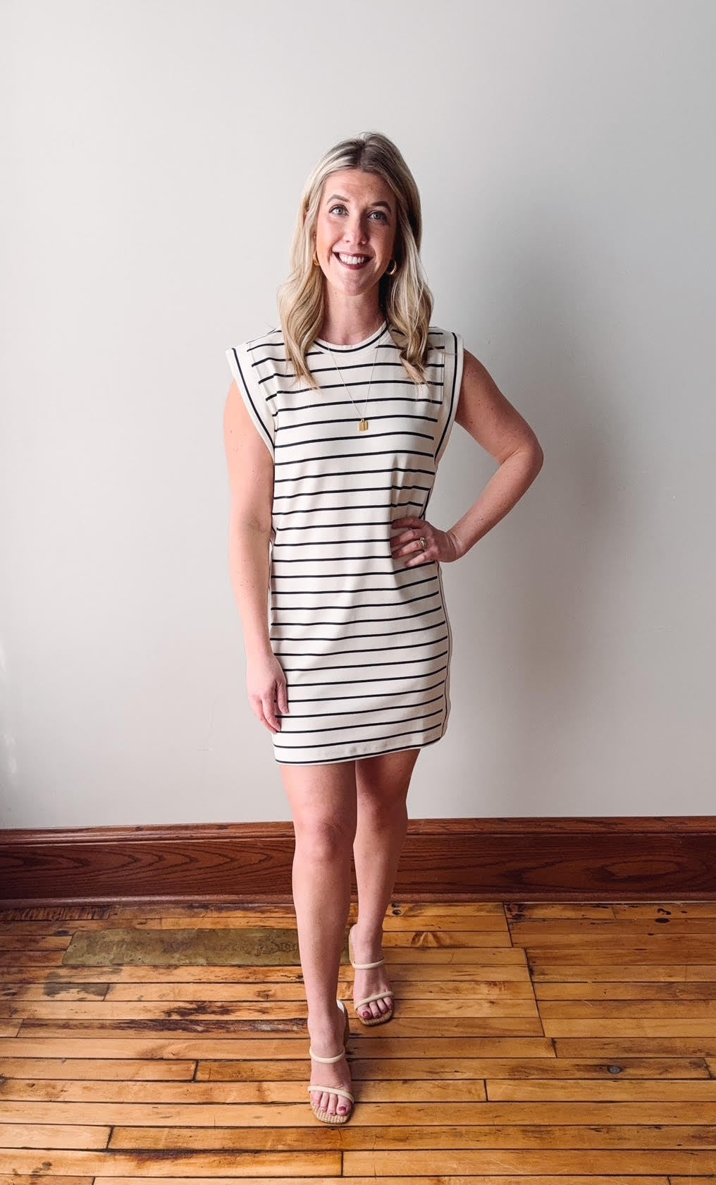 Woman wearing a black and white striped dress standing on a wooden floor with a white wall background