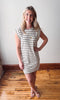 Woman wearing a striped dress standing on a wooden floor with a white wall background