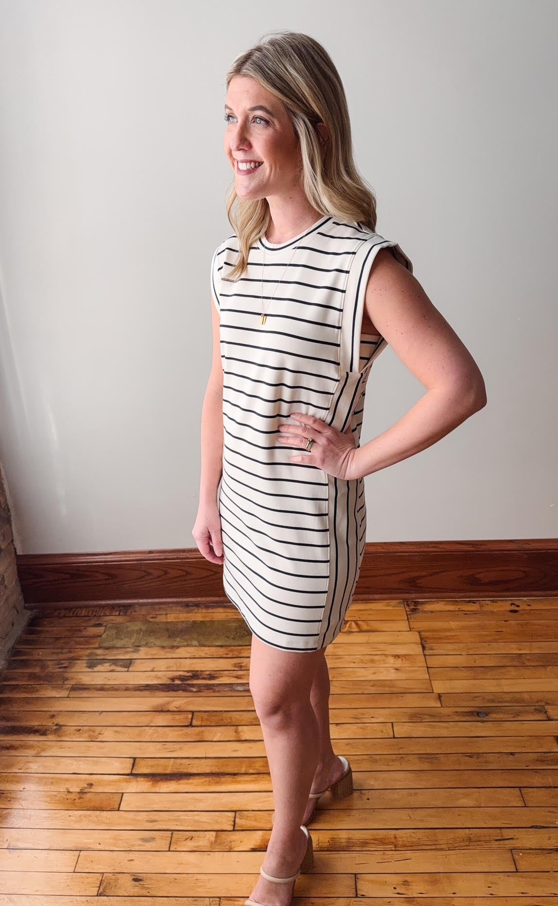 Woman wearing a striped dress standing on a wooden floor with a white wall background