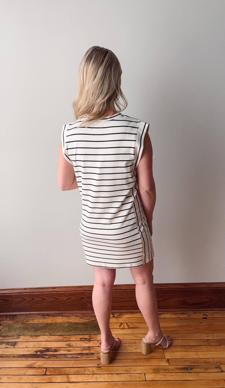 Woman wearing a black and white striped dress standing on a wooden floor against a plain wall.