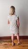 Woman wearing a black and white striped dress standing on a wooden floor against a plain wall.