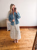 Woman taking a mirror selfie wearing a floral dress and denim jacket in a room with wooden flooring.
