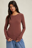 Woman wearing a brown long-sleeve top and blue jeans against a beige background
