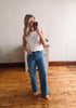 Woman taking a mirror selfie wearing a white lace top and blue jeans in a room with wooden flooring.