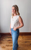 Woman wearing a white blouse and blue jeans standing in a room with wooden flooring.