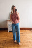 Woman taking a mirror selfie wearing a pink sleeveless shirt and blue jeans in a room with wooden flooring.