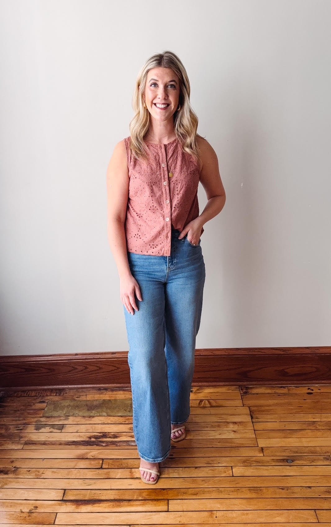 Woman wearing a pink sleeveless top and blue jeans standing on a wooden floor.