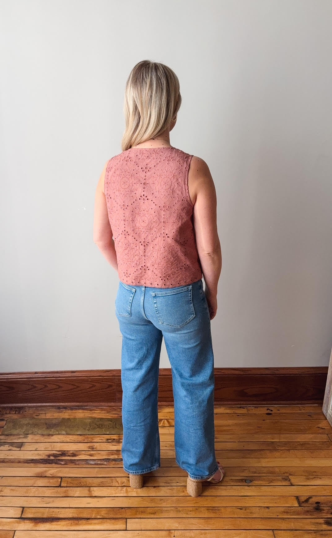 Person wearing a pink sleeveless top and blue jeans standing on a wooden floor.