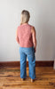 Person wearing a pink sleeveless top and blue jeans standing on a wooden floor.
