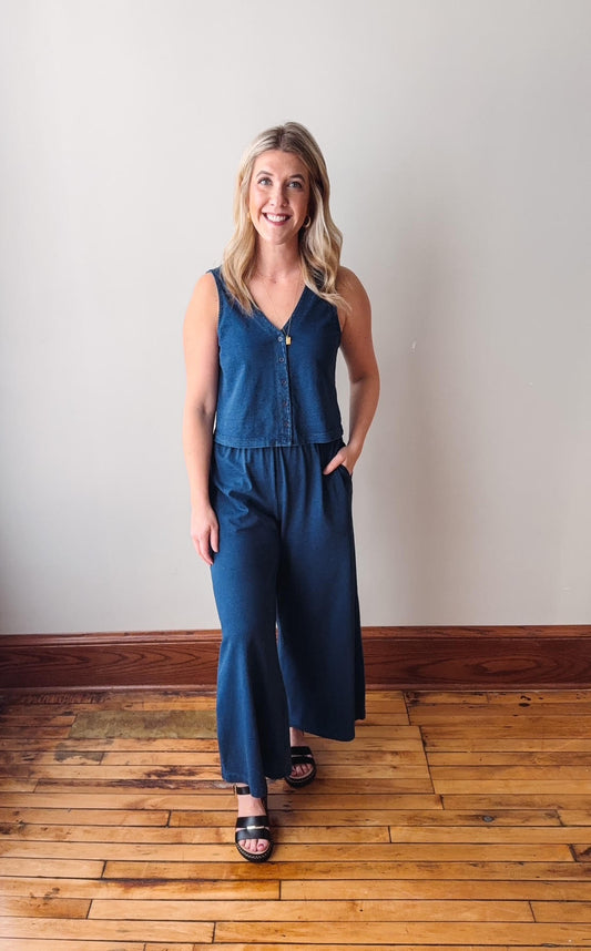 Woman wearing a blue jumpsuit standing on a wooden floor with a white wall background