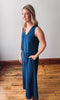 Woman wearing a blue jumpsuit standing on a wooden floor with a white wall background