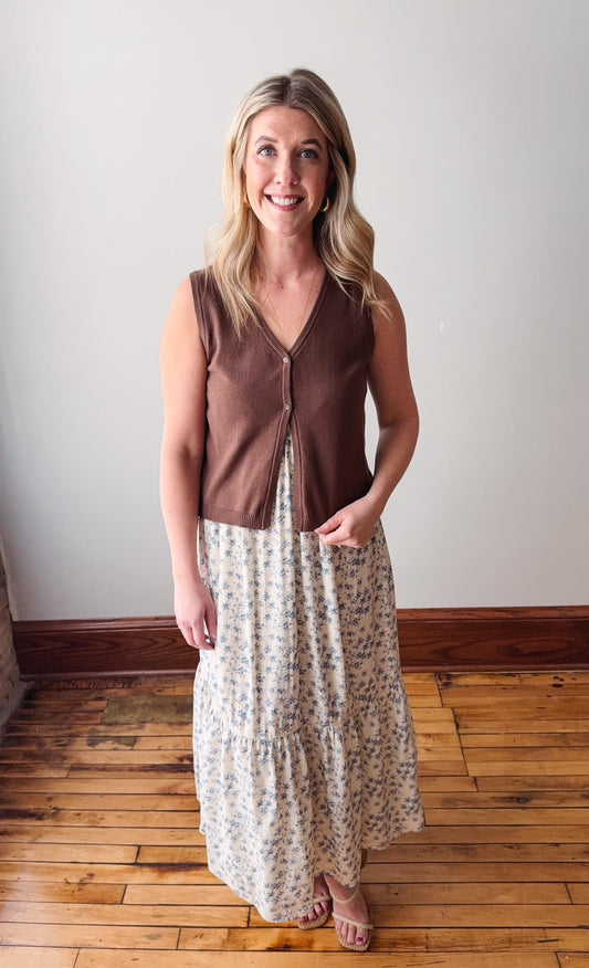 Woman wearing a brown sleeveless top and floral skirt standing on a wooden floor.