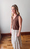 Woman wearing a brown sleeveless top and floral dress standing on a wooden floor.