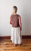 Person wearing a brown sleeveless top and white floral skirt standing on a wooden floor.