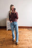 Woman taking a mirror selfie wearing a maroon sweater and light blue jeans in a room with wooden flooring.