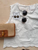 White blouse with black sunglasses, earrings, and a brown purse on a wooden surface