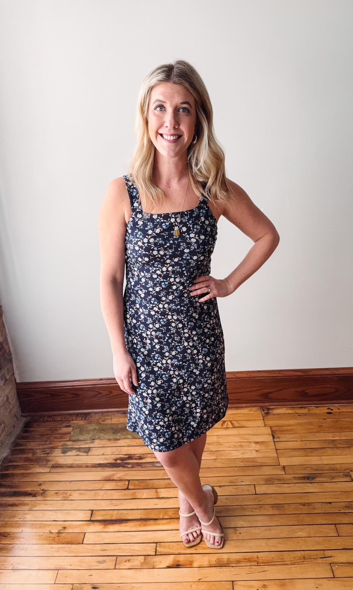 Woman wearing a floral dress standing on a wooden floor with a white wall background