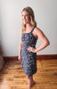 Woman wearing a navy floral dress standing in a room with wooden flooring and a white wall.