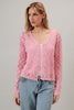 Woman wearing a pink lace cardigan over a white top and blue jeans on a gray background